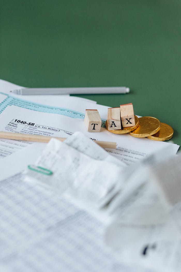 Tax forms, coins, and block letters spelling TAX on a green background, symbolizing finance.